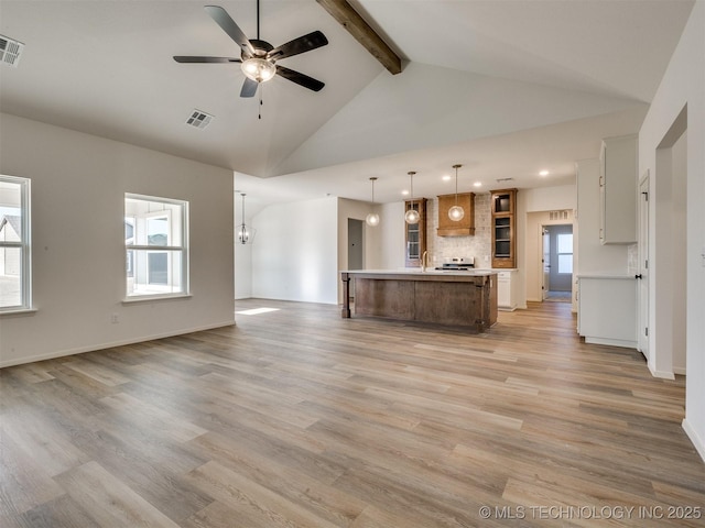 unfurnished living room with a wealth of natural light, visible vents, beamed ceiling, and ceiling fan with notable chandelier