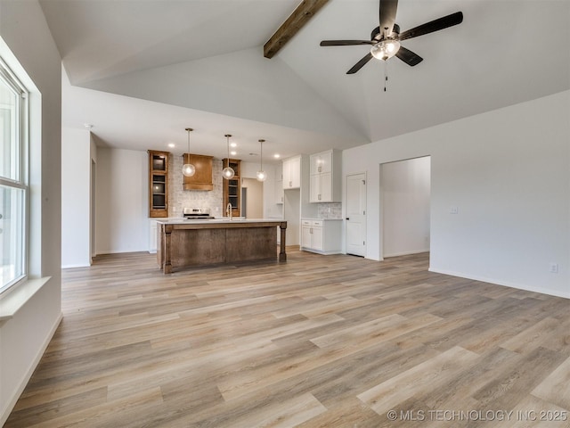 unfurnished living room with ceiling fan, beamed ceiling, light wood finished floors, and a sink