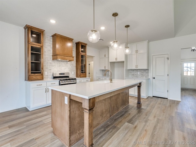 kitchen with light wood finished floors, stainless steel range with gas stovetop, glass insert cabinets, and wall chimney range hood