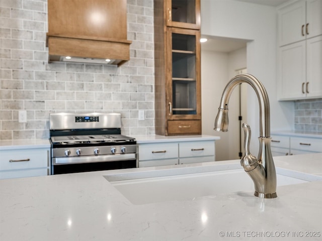 kitchen with decorative backsplash, glass insert cabinets, stainless steel range with gas stovetop, and custom range hood