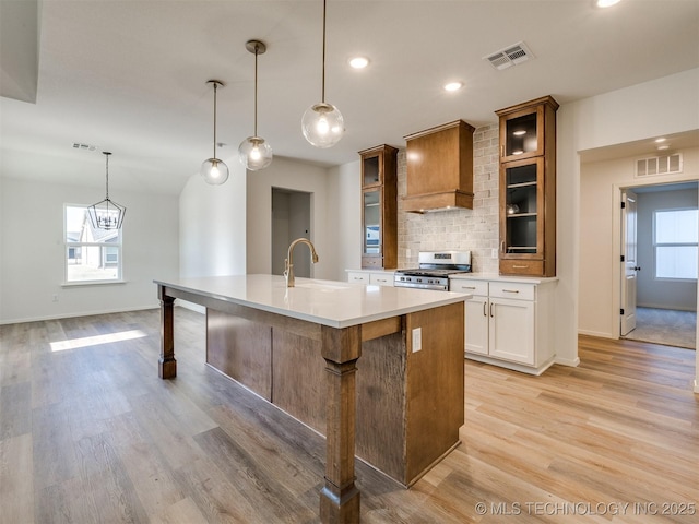 kitchen with gas stove, a center island with sink, visible vents, a sink, and backsplash