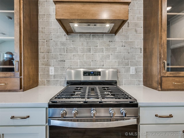 kitchen featuring stainless steel gas stove, tasteful backsplash, custom exhaust hood, and light countertops