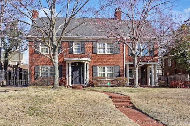 georgian-style home with a front lawn, brick siding, a chimney, and a gate