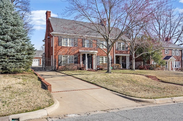 view of front of home featuring a front yard, a gate, brick siding, and a chimney