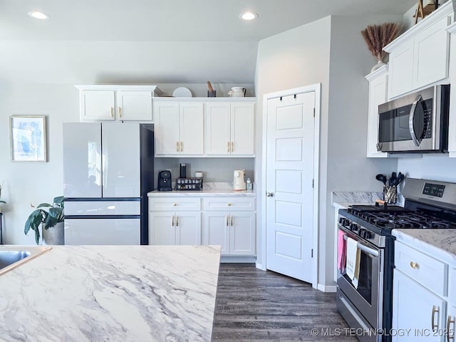 kitchen with dark wood-style floors, appliances with stainless steel finishes, white cabinetry, and light stone counters