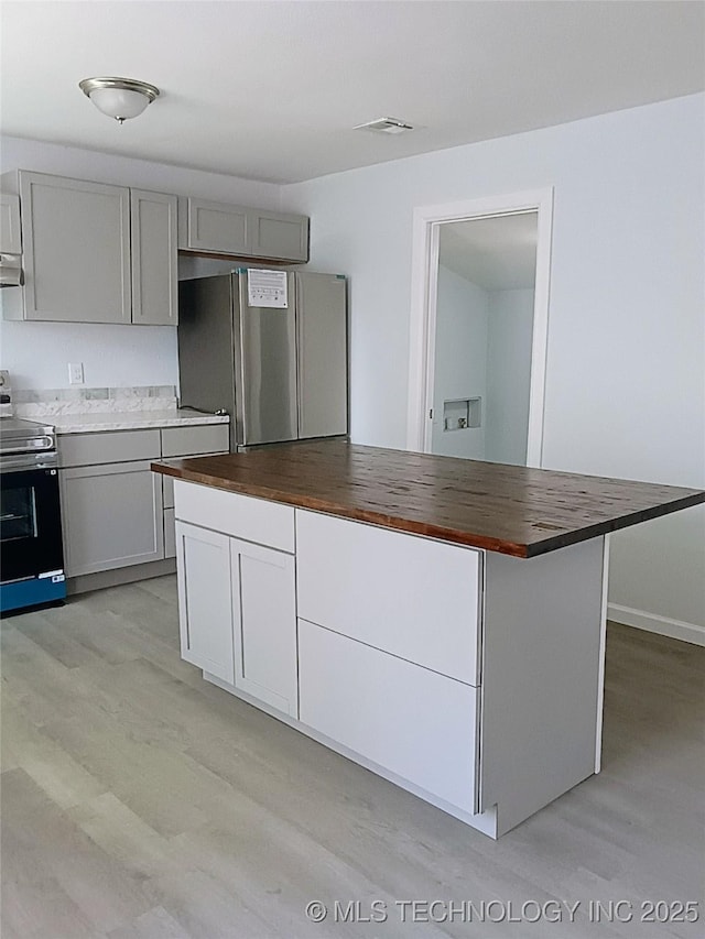 kitchen with stainless steel appliances, gray cabinets, light wood-style flooring, and butcher block counters