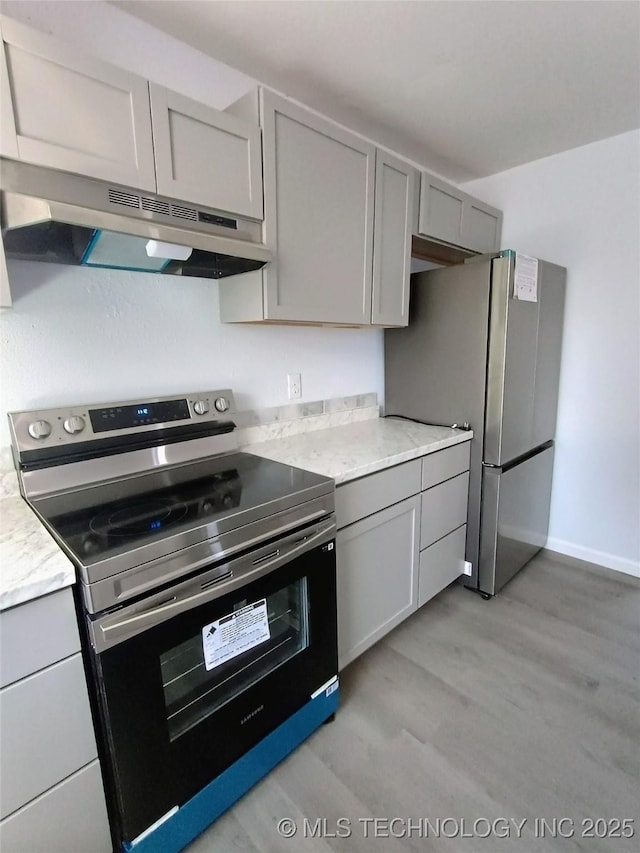 kitchen featuring gray cabinetry, light wood-style flooring, under cabinet range hood, stainless steel appliances, and baseboards