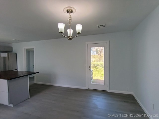 unfurnished dining area with visible vents, baseboards, an inviting chandelier, and dark wood-style floors