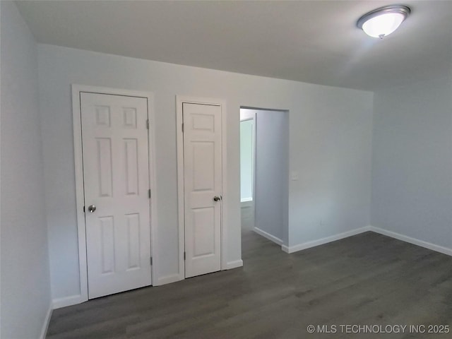 unfurnished bedroom with baseboards and dark wood-type flooring