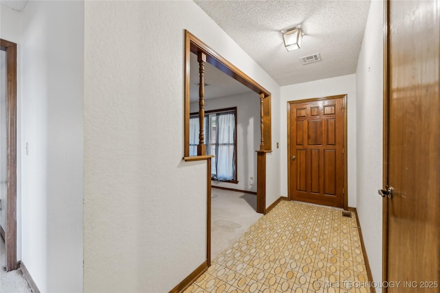 hall featuring baseboards, visible vents, a textured wall, and a textured ceiling