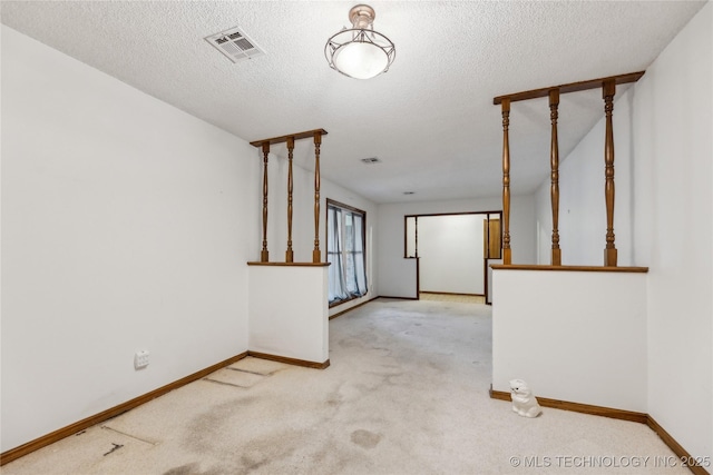 carpeted empty room with visible vents, a textured ceiling, and baseboards