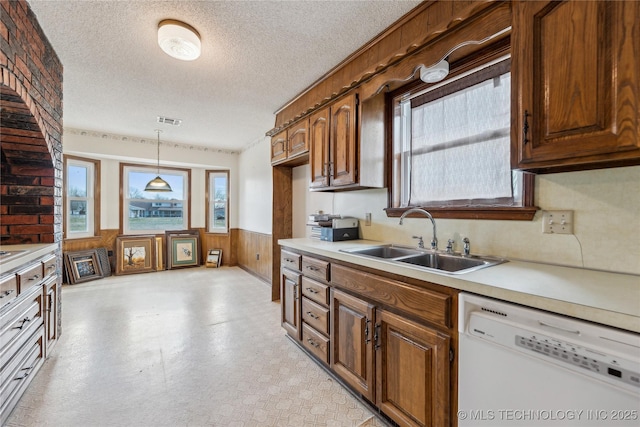 kitchen featuring light floors, a wainscoted wall, a sink, light countertops, and dishwasher