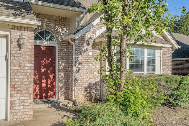 doorway to property with a garage, brick siding, and a shingled roof