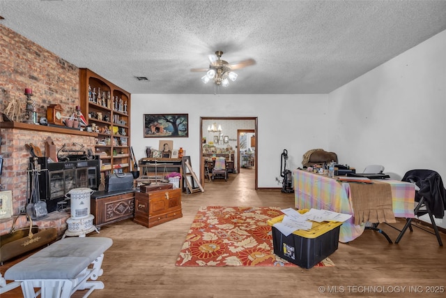 living area with baseboards, ceiling fan, a fireplace, wood finished floors, and a textured ceiling