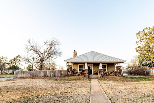 bungalow featuring metal roof, a porch, a chimney, and fence