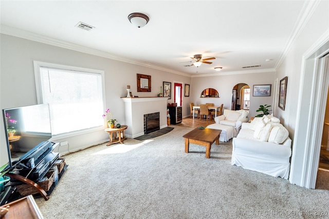 carpeted living area featuring arched walkways, visible vents, crown molding, and a fireplace with flush hearth