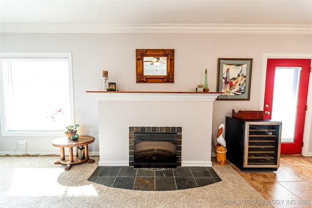 tiled living room featuring crown molding, wine cooler, a fireplace with flush hearth, and baseboards