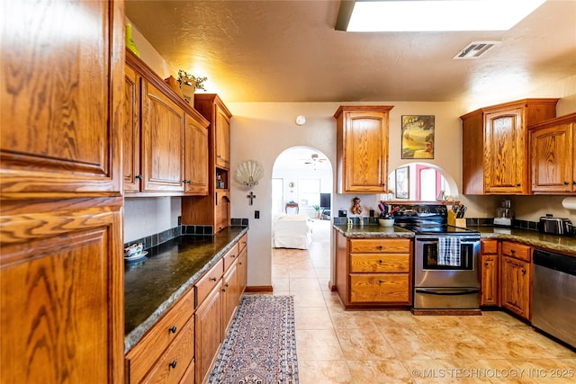 kitchen with visible vents, brown cabinetry, light tile patterned flooring, arched walkways, and stainless steel appliances