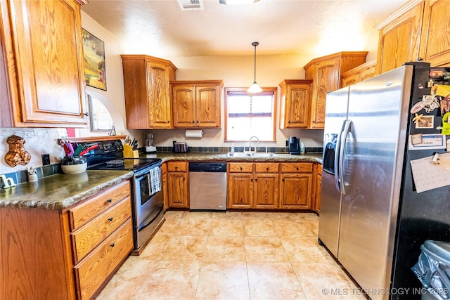 kitchen with a sink, dark countertops, appliances with stainless steel finishes, brown cabinetry, and hanging light fixtures