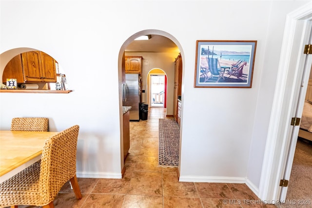 hallway with arched walkways, light tile patterned floors, and baseboards