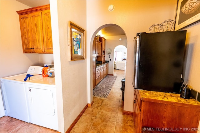 laundry area featuring baseboards, light tile patterned flooring, arched walkways, cabinet space, and separate washer and dryer