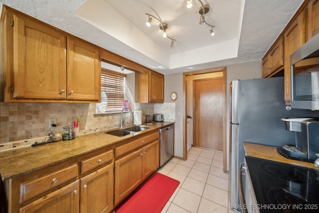 kitchen with a sink, a tray ceiling, brown cabinets, and appliances with stainless steel finishes