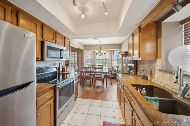 kitchen featuring brown cabinetry, a tray ceiling, light tile patterned flooring, a sink, and appliances with stainless steel finishes