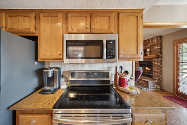 kitchen featuring decorative backsplash, a brick fireplace, appliances with stainless steel finishes, and brown cabinetry