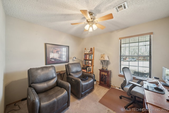 office area with a textured ceiling, light colored carpet, visible vents, and ceiling fan