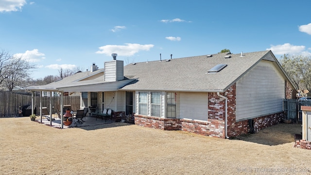 back of house with a fenced backyard, roof with shingles, brick siding, a chimney, and a patio area