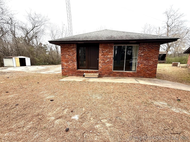 rear view of house featuring an outbuilding, brick siding, and roof with shingles