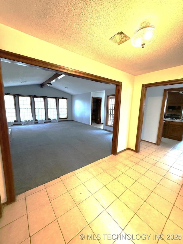 empty room with a textured ceiling, vaulted ceiling with beams, light tile patterned floors, and light carpet