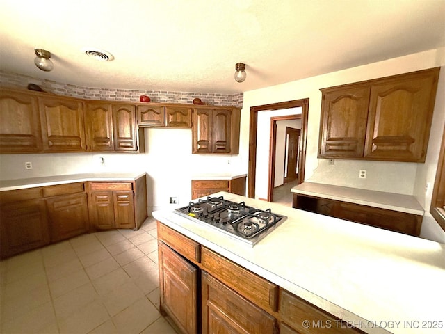 kitchen featuring visible vents, stainless steel gas cooktop, light tile patterned flooring, light countertops, and brown cabinets