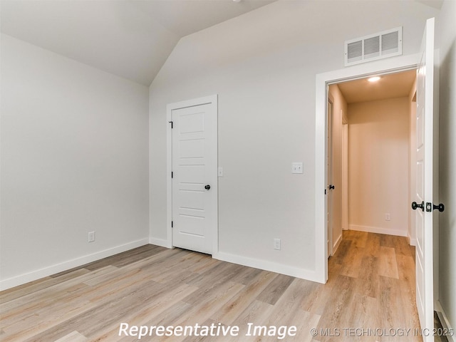 unfurnished bedroom featuring lofted ceiling, baseboards, visible vents, and light wood finished floors