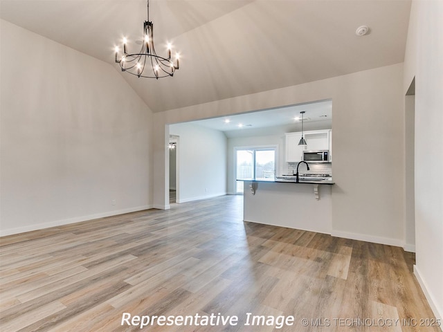 unfurnished living room with light wood finished floors, a notable chandelier, baseboards, and vaulted ceiling