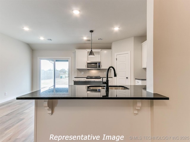 kitchen with a breakfast bar, a sink, white cabinetry, stainless steel microwave, and backsplash