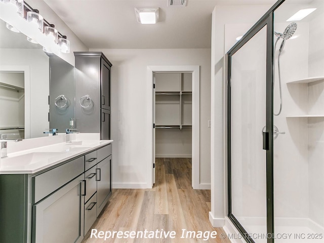 full bath featuring a walk in closet, visible vents, wood finished floors, a shower stall, and double vanity