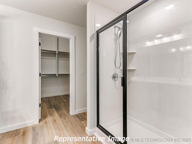 bathroom with a spacious closet, a stall shower, baseboards, and wood finished floors