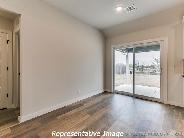 spare room with vaulted ceiling, visible vents, baseboards, and wood finished floors