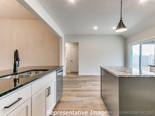 kitchen featuring dark stone counters, light wood-style flooring, a sink, dishwasher, and decorative light fixtures