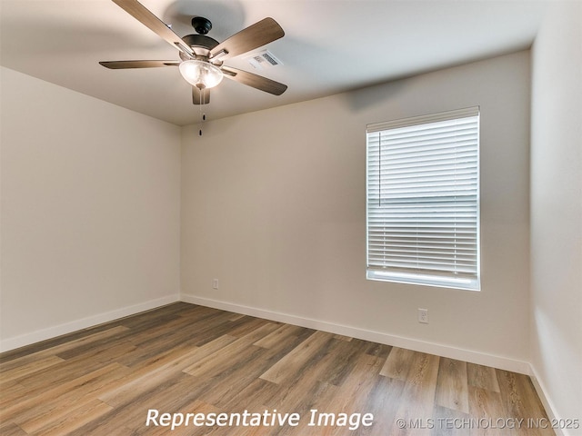 spare room with ceiling fan, visible vents, baseboards, and wood finished floors