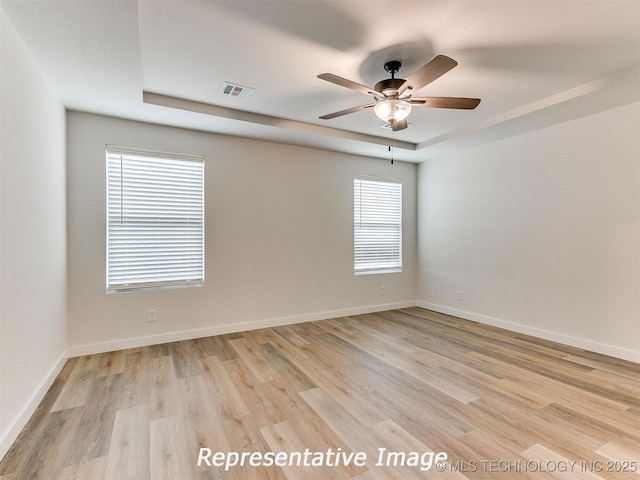 unfurnished room with a raised ceiling, light wood-style floors, visible vents, and baseboards