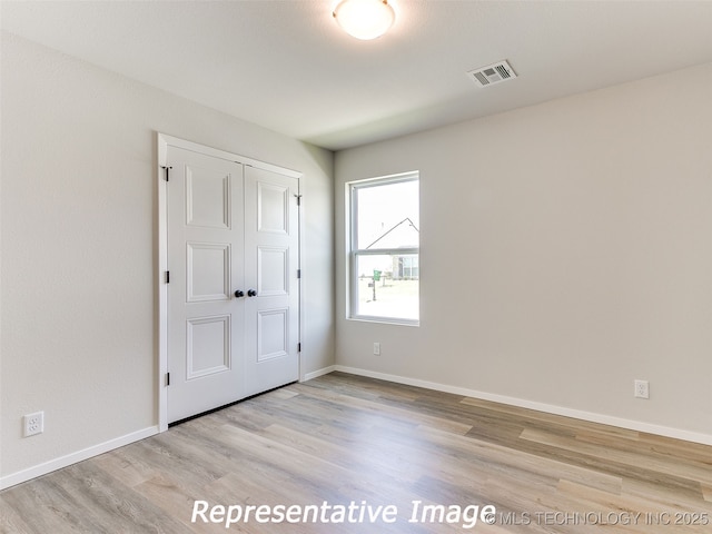 unfurnished bedroom featuring wood finished floors, visible vents, a closet, and baseboards