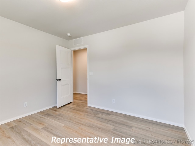 empty room with wood finished floors, visible vents, and baseboards