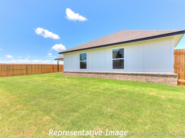 rear view of property with a lawn, roof with shingles, and fence