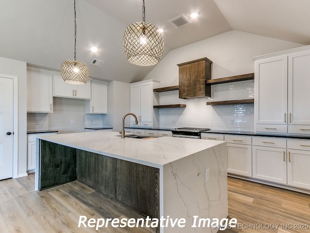 kitchen with visible vents, open shelves, stainless steel range with gas stovetop, white cabinets, and a sink