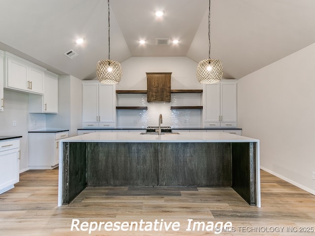 kitchen featuring open shelves, visible vents, a center island with sink, and a sink