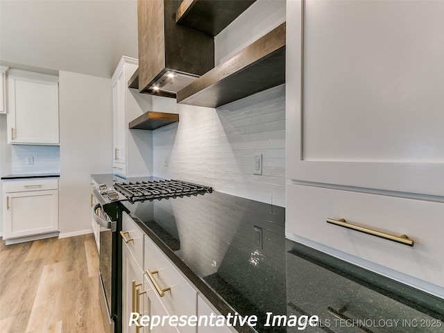 kitchen featuring tasteful backsplash, dark stone counters, gas range oven, light wood-style floors, and white cabinetry