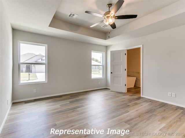 unfurnished bedroom featuring visible vents, baseboards, a tray ceiling, and wood finished floors