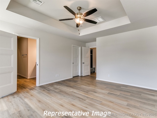 unfurnished bedroom with light wood-style flooring, a raised ceiling, and baseboards